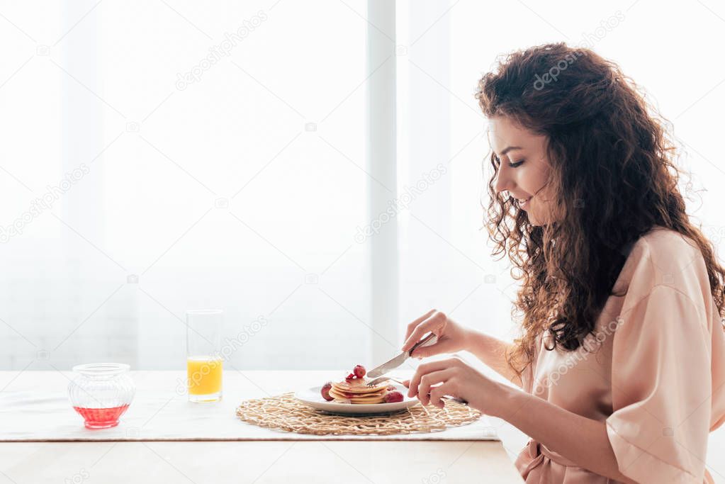 side view of smiling girl eating pancakes in kitchen