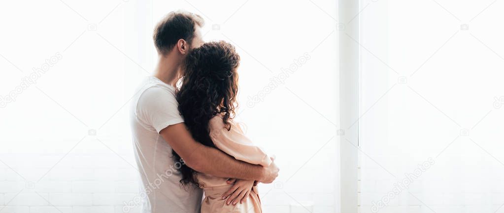 panoramic shot of man embracing girlfriend and looking away