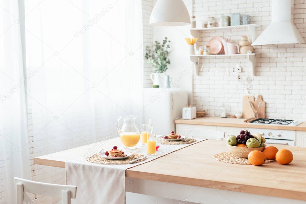 served table with pancakes, fruits and orange juice in kitchen