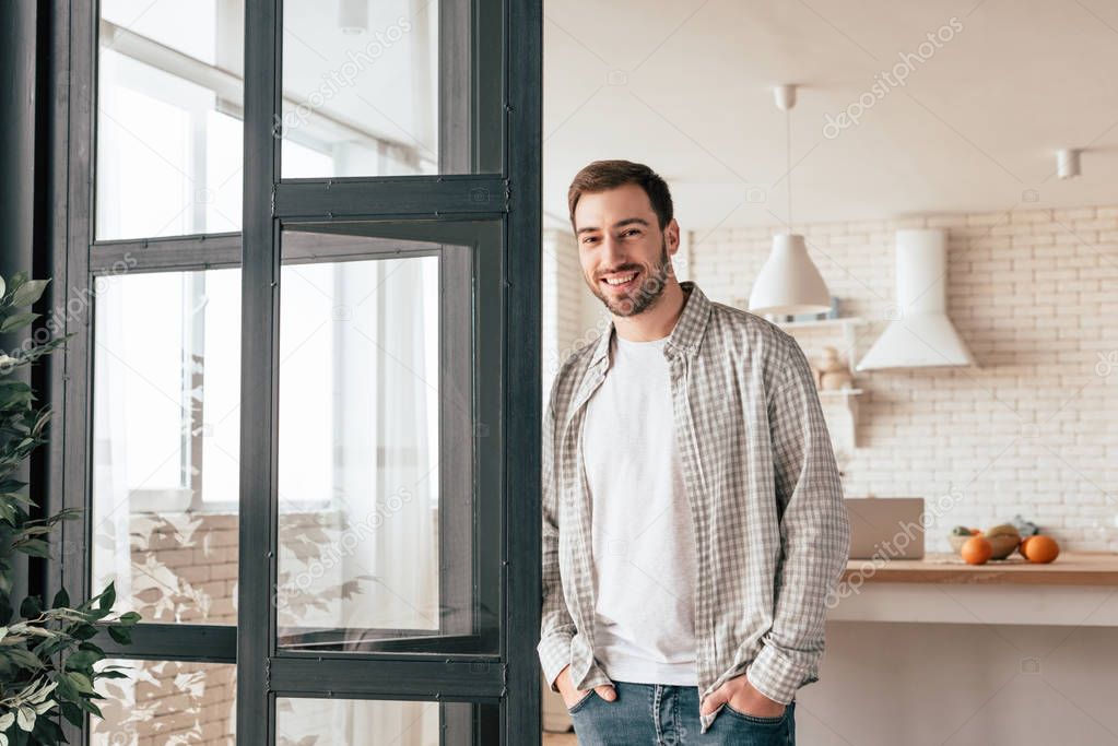 smiling bearded man standing with hands in pockets and looking at camera