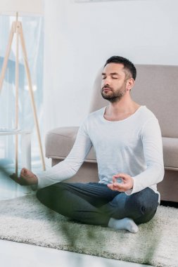 Lotus Pose halı üzerinde oturan ve evde meditasyon yakışıklı adam seçici odak