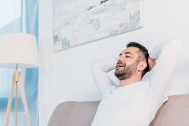 gözleri kapalı yakışıklı sakallı adam ve Eller Arka arkaya kopya alanı ile evde kanepede istirahat