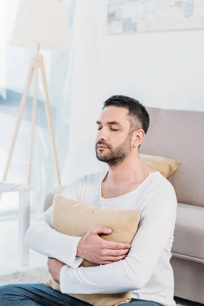 Knappe Man Met Ogen Gesloten Zittend Tapijt Knuffelen Kussen Thuis — Stockfoto