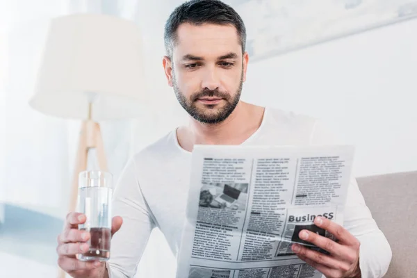 Snygg Skäggiga Man Sitter Med Glas Vatten Och Läser Tidningen — Stockfoto