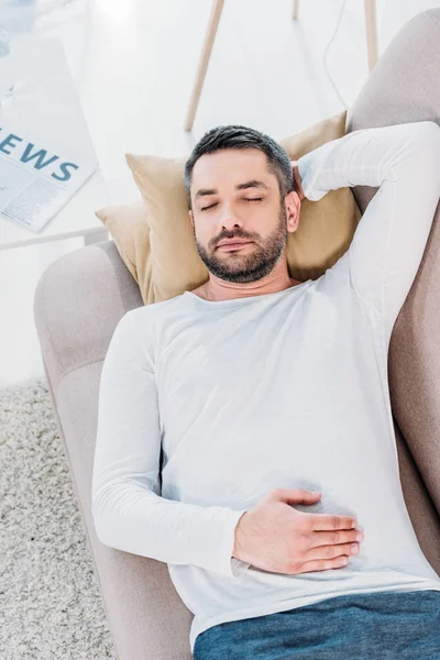 top view of handsome bearded man with eyes closed resting on couch at home