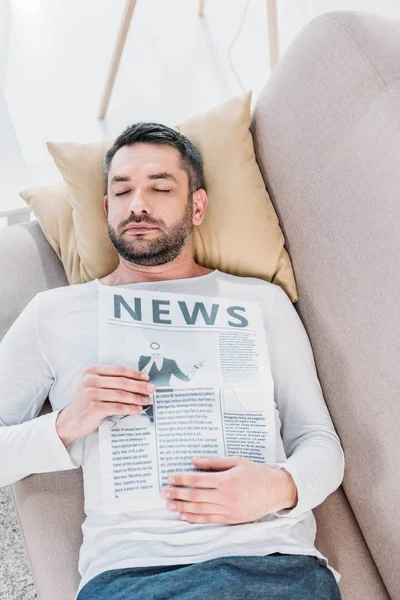 英俊的胡子男子闭上眼睛拿着报纸 并在家里的沙发上休息 — 图库照片