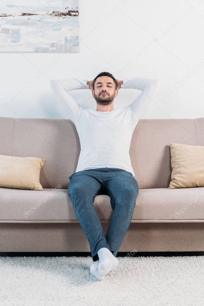 handsome bearded man with eyes closed and Hands Behind Back resting on couch at home