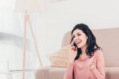 güzel gülümseyen kadın gesturing ve kopya alanı ile evde akıllı telefon konuşuyor
