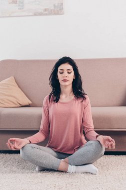 Gözleri Lotus 'ta kapalı güzel bir kadın. Evde oturma odasında meditasyon yapıyor. 