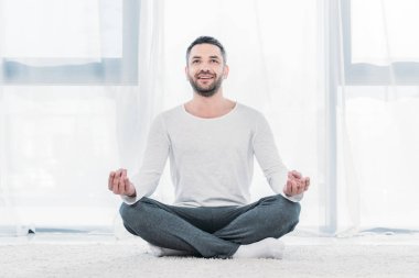 mutlu yakışıklı adam Lotus Pose halı üzerinde oturan ve evde meditasyon