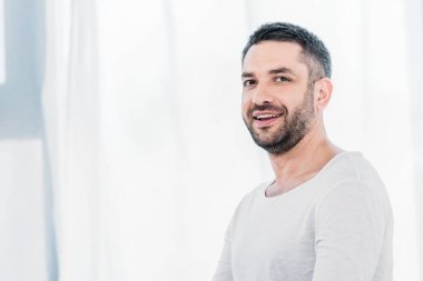 yakışıklı sakallı adam kamera bakıyor ve güneş ışığı ve kopyalama alanı ile evde gülümseyen