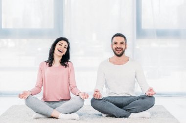 happy woman and man sitting in Lotus Pose and meditating at home clipart