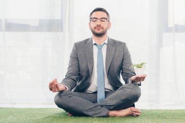 Lotus Pose otururken çim mat meditasyon gözlüklü işadamı 