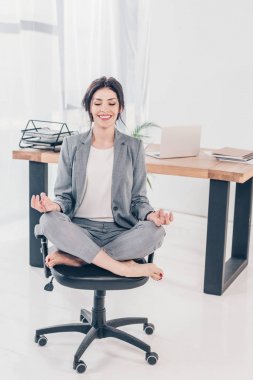 takım elbise güzel gülümseyen iş kadını sandalyede oturan ve ofiste Lotus Pose meditasyon