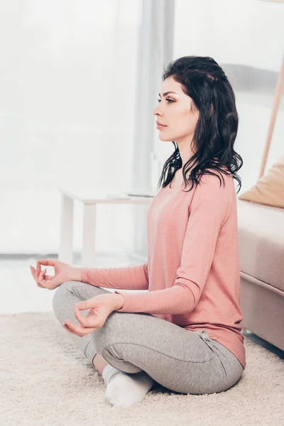 リビングルームで自宅で瞑想を練習ロータスポーズの美しい女性 — ストック写真