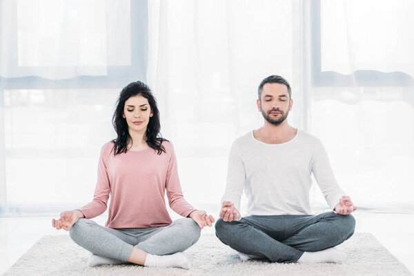 женщина и мужчина с закрытыми глазами сидят в Lotus Pose и медитируют дома
