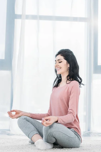 自宅のリビングルームで瞑想を練習ロータスポーズの美しい笑顔の女性 — ストック写真