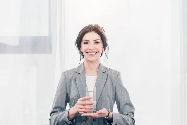 Piękny Uśmiechnięty Bizneswoman Garniturze Trzymając Szklankę Wody Patrząc Aparat — Zdjęcie stockowe