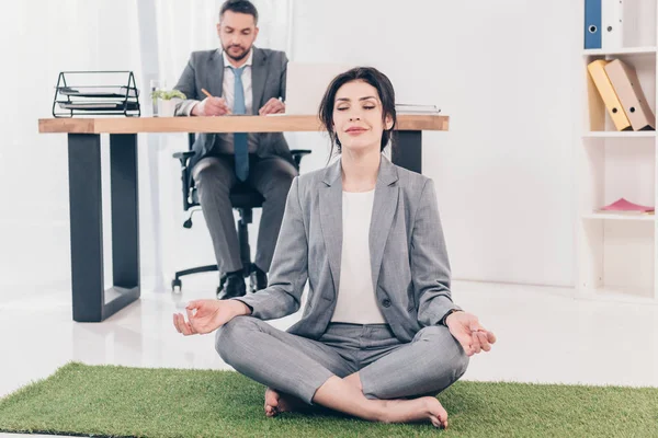 Obchodní Žena Meditující Lotus Pose Travní Rohoži Zatímco Obchodník Sedí — Stock fotografie