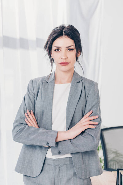 beautiful confident businesswoman in suit with crossed arms looking at camera in office
