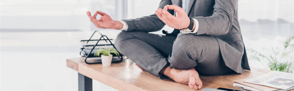 панорамный снимок бизнесмена, медитирующего в Lotus Pose на рабочем столе
