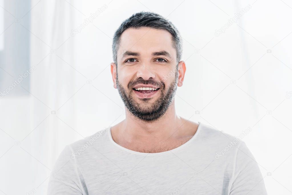handsome bearded man looking at camera and smiling at home with sunlight and copy space