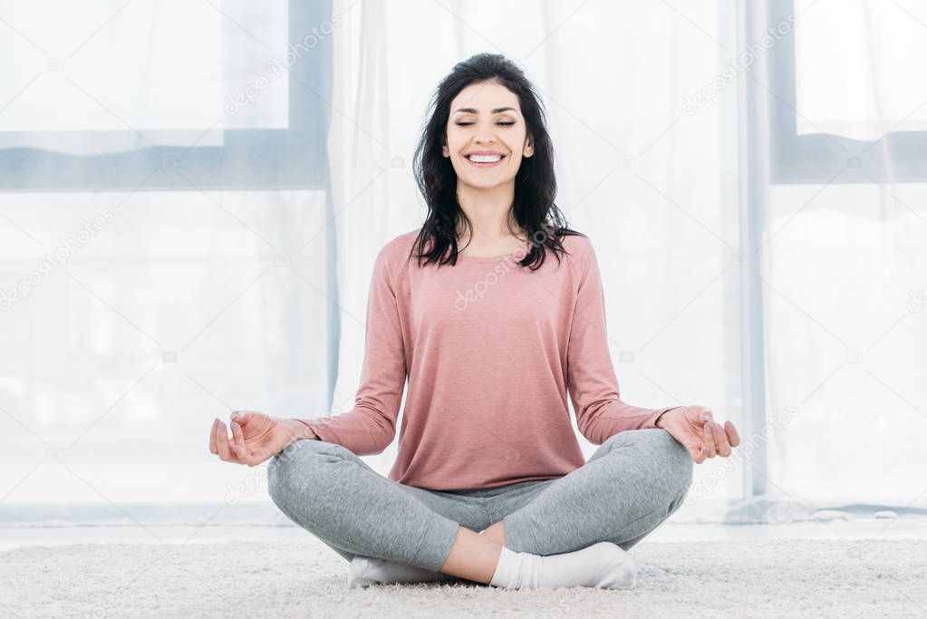 beautiful smiling woman in Lotus Pose practicing meditation in Living Room at home 