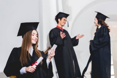 öğrencilerin yanında diploma tutarken akıllı telefon bakarak çekici kız seçici odak 