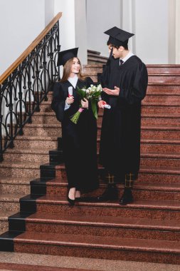diploma tutarken çekici kız ile konuşurken mezuniyet kap gesturing mutlu adam 