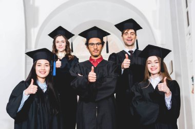 mezuniyet önlükleri neşeli öğrenciler ayakta ve başparmak gösteren