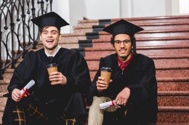 diploma ve kağıt bardak tutan mezuniyet kapakları neşeli öğrenciler 