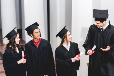 mezuniyet önlükleri öğrencilerin yanında gesturing neşeli adam ve diploma tutarak 