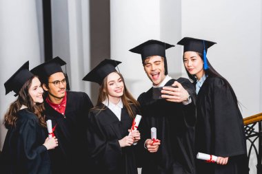 mezuniyet önlükneşeli öğrenciler diplomaları tutarken selfie ve gülümseyerek 