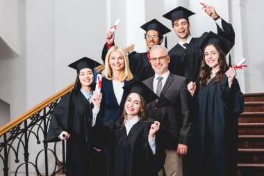 mutlu öğretmenlerin yakınında diploma tutan mezuniyet kapakları neşeli öğrenciler 