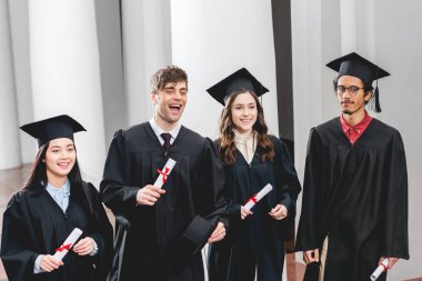 smiling group on students in graduation gowns holding diplomas  clipart