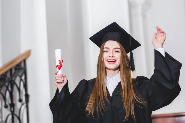 Wesoła Młoda Kobieta Posiadających Dyplom Machając Ręką Uniwersytecie — Zdjęcie stockowe