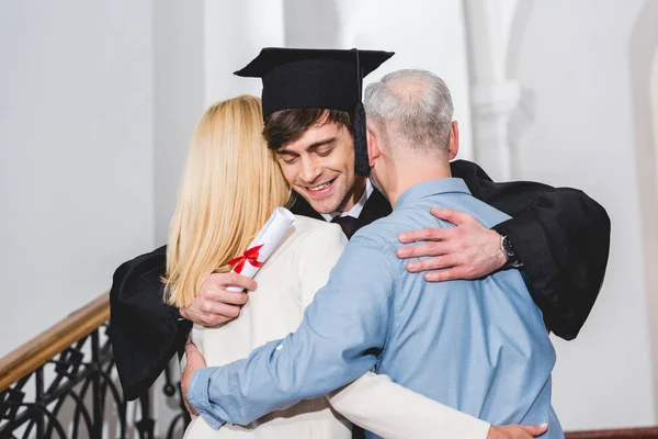 Cheerful Son Graduation Cap Holding Diploma While Hugging Parents — Stock Photo, Image