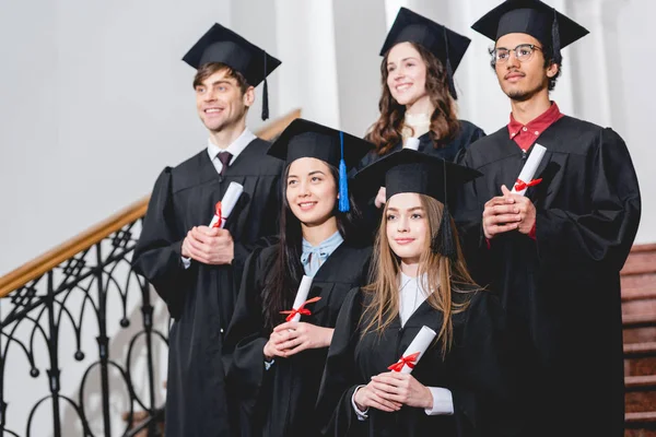 穿着毕业礼服的开朗学生在大学里持有文凭 — 图库照片