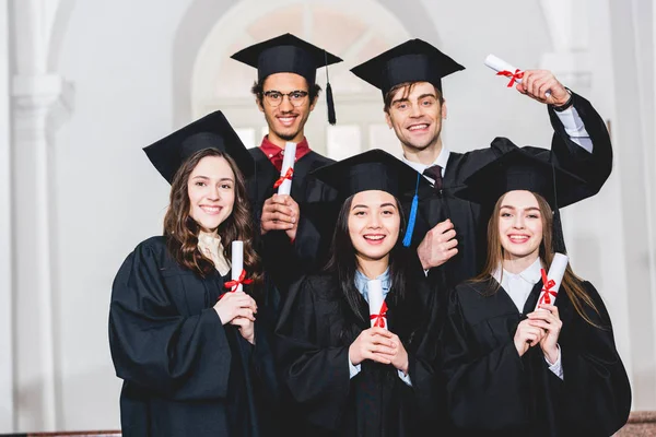 Szczęśliwa Grupa Studentów Suknie Dyplomowe Uśmiechnięty Posiadania Dyplomów — Zdjęcie stockowe