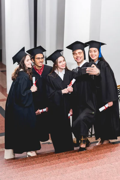 Счастливые Студенты Выпускных Платьях Делают Селфи Улыбаются Держа Дипломы — стоковое фото