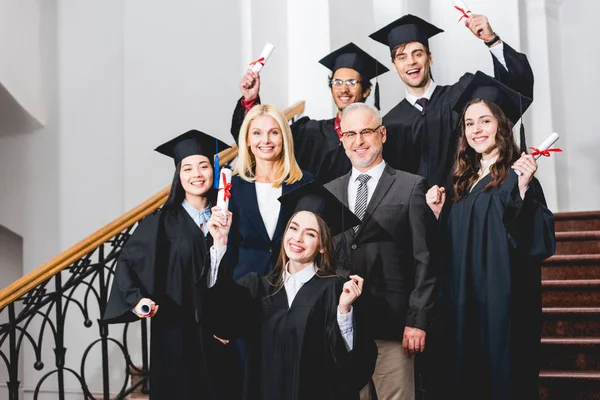 Radosnych Uczniów Kapitalikami Dyplomów Pobliżu Szczęśliwych Nauczycieli — Zdjęcie stockowe