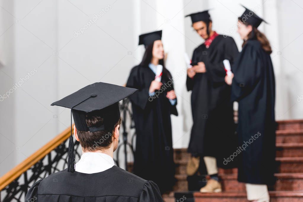back view of student in graduation cap standing in university 