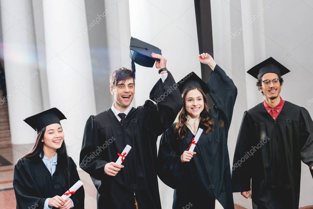 happy group on students gesturing and celebrating graduation while holding diplomas 