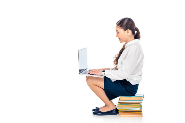 schoolgirl in formal wear sitting on books and using laptop Isolated On White with copy space