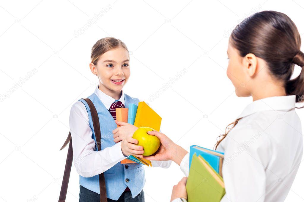 schoolgirls in formal wear with books looking at each other and sharing apple Isolated On White