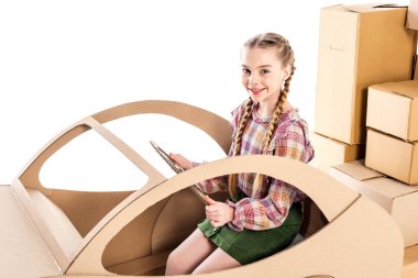 happy kid looking at camera and holding steering wheel while playing with cardboard car Isolated On White clipart