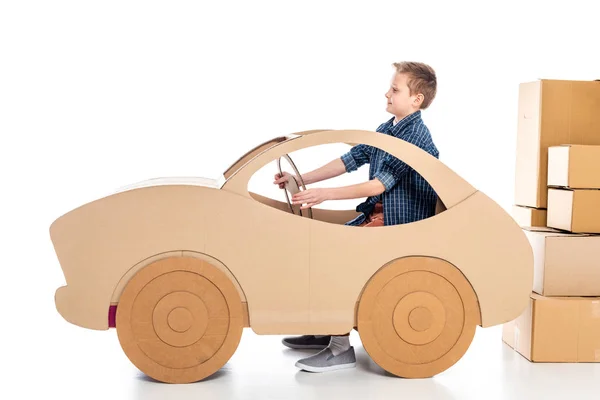 boy sitting in cardboard car and holding steering wheel on white