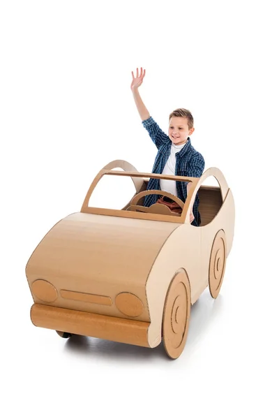 smiling boy sitting in cardboard car and waving on white