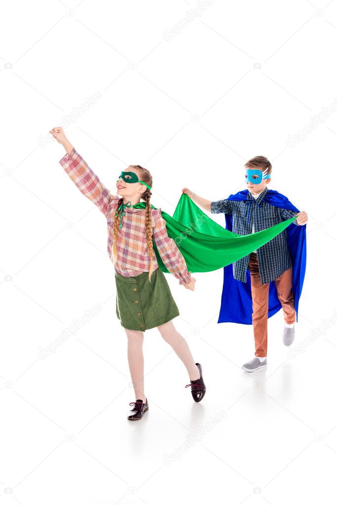 boy holding cape of kid in superhero costume posing with outstretched hand On White