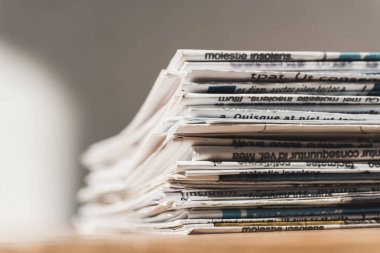 selective focus of different print newspapers in pile on wooden table 